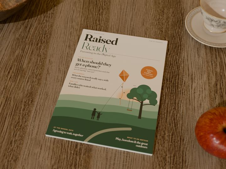 Issue 1 of Raised Ready lying on a wooden kitchen table next to a teacup and an apple